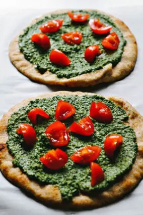 Pesto-Pizza mit sonnengetrockneten Tomaten, Oliven und Rucola
