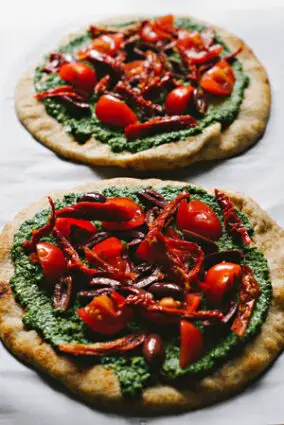 Pesto-Pizza mit sonnengetrockneten Tomaten, Oliven und Rucola