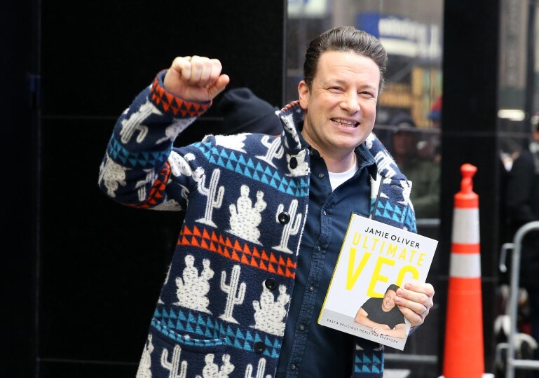 Jamie Oliver holding one of his recipe cookbooks.
